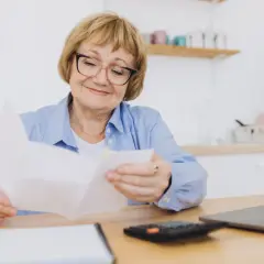 Uśmiechnięta starsza pani analizuje dokumenty, zastanawiając się nad tym, jaka emerytura z KRUS po 10 latach będzie jej przysługiwać.