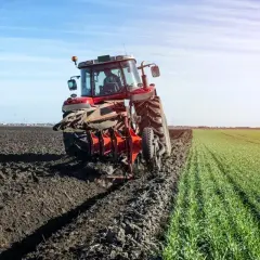 Aktywny rolnik orze pole czerwonym traktorem, przygotowując ziemię pod nowe uprawy. Wsparcie z dopłat pozwala na efektywne gospodarowanie.