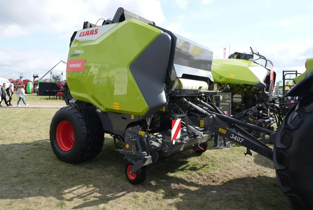 Zielona prasa Claas 780 RC Ceres z dużymi kołami, gotowa do tworzenia balotów. Obok inne maszyny rolnicze.