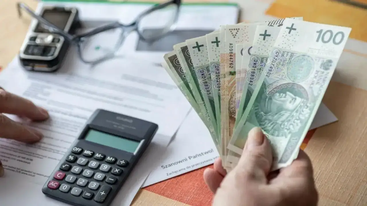Ręka trzyma banknoty 100 zł, obok kalkulator i dokumenty. Może to być rozliczenie podatku rolnego.