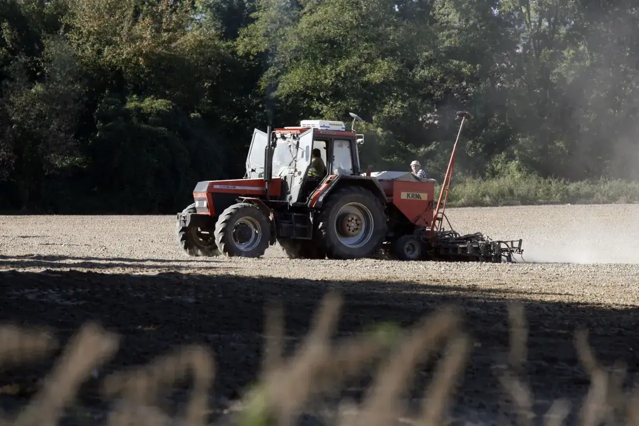 Czerwony traktor z siewnikiem pracuje na polu. Rolnik w kabinie, myśląc o przyszłości i swoim prawie do emerytury rolniczej według nowych zasad.